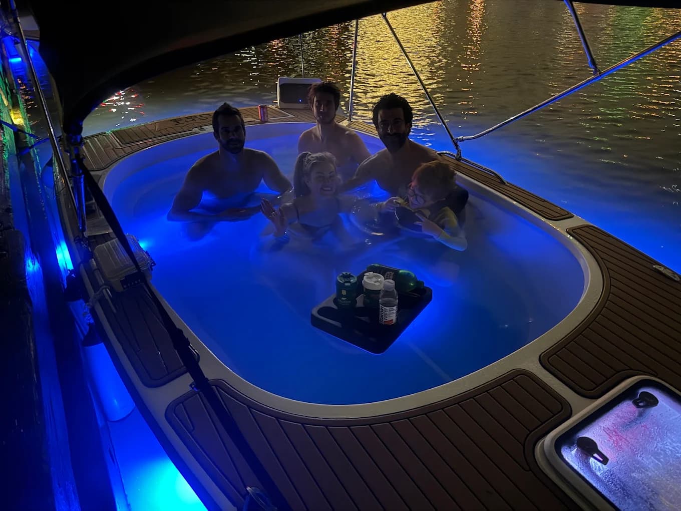Hot tub boat after dark with the underwater LED lights glowing blue and guests soaking with drinks on a floating tray